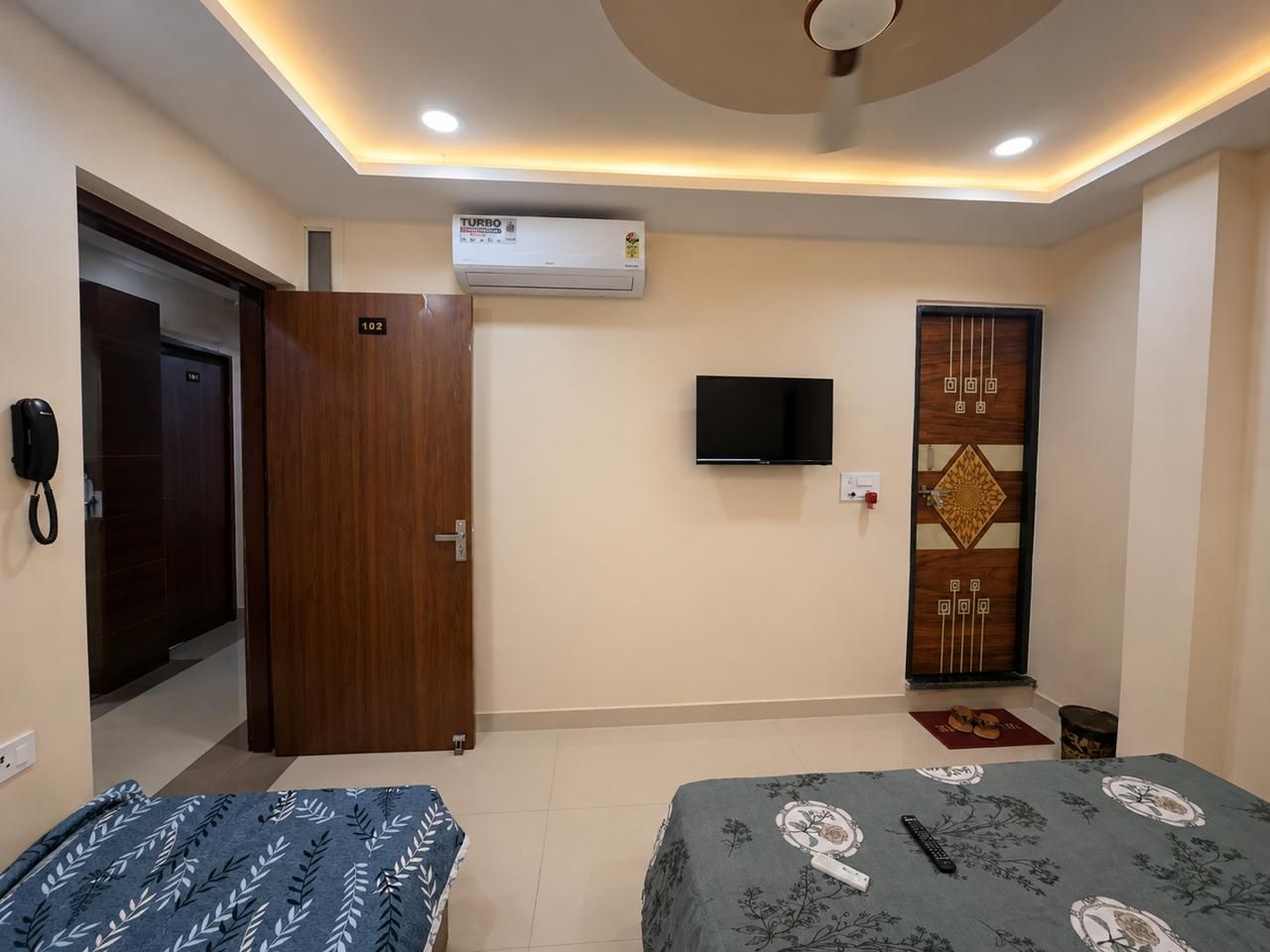 A hotel room with a bed, a TV, an air conditioner, and a door.