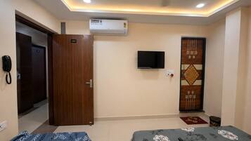 A hotel room with a bed, a TV, an air conditioner, and a door.
