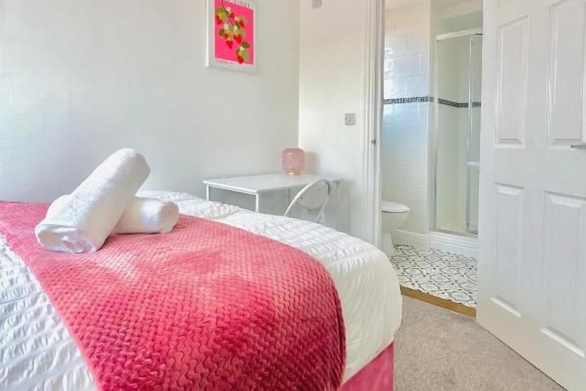 Un dormitorio con cama, mesita de noche, una silla y una puerta que da a un baño.