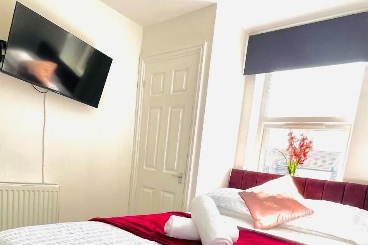 Una habitación de hotel con cama, televisor montado en la pared, ventana con vistas y una puerta.