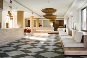 Rebedor d'hotel amb sòl de pissareta, una taquilla d'admissió, zona de seients amb sofàs i làmpades de vimet.