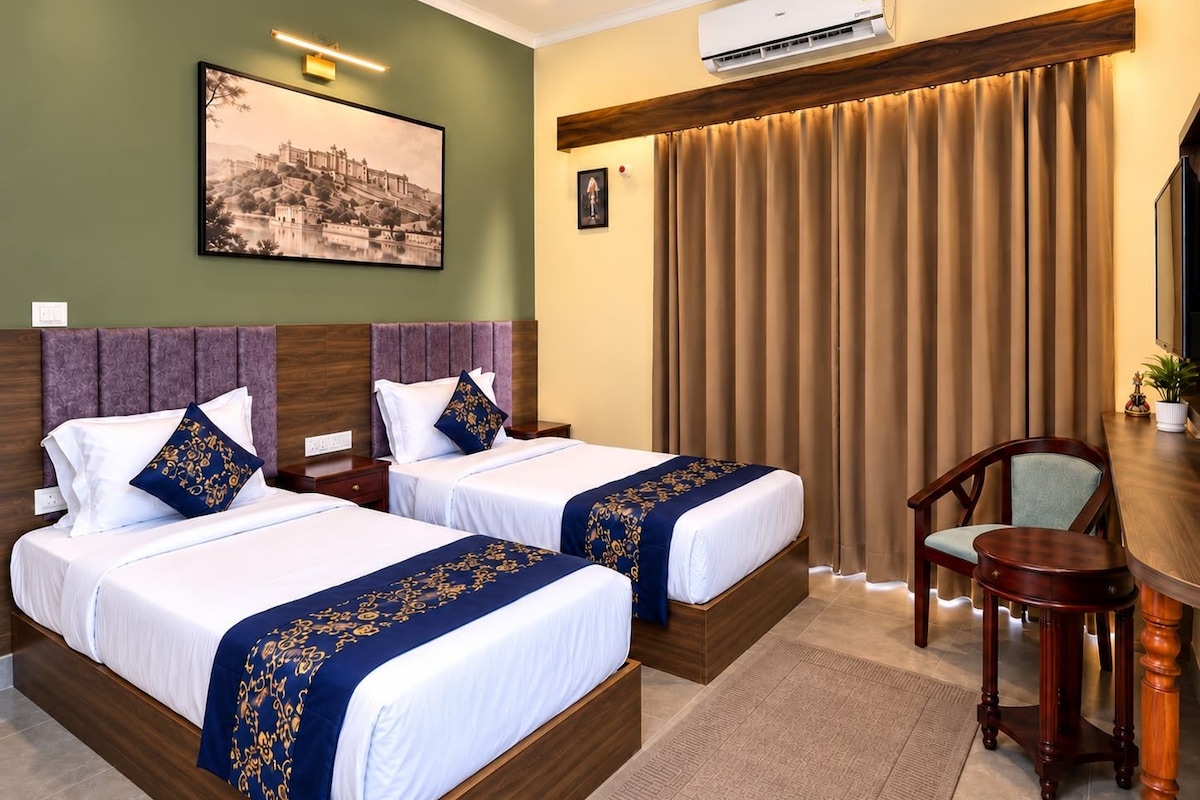 A hotel room with two beds, a desk, a chair, an air conditioning unit, a ceiling fan, and a painting on the wall.