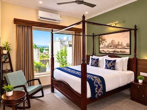 A four-poster bed with a canopy, a chair, a bedside table, and a nightstand. - The OG Stays (Jaipur)