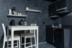 Ett kompakt kök med ett vitt bord, två stolar, en kaffemaskin och en svart diskmaskin.