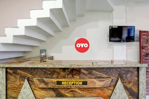 Un mostrador de recepción con encimera de mármol y un cartel que dice 'RECEPTION', una escalera y un televisor fijado a la pared.
