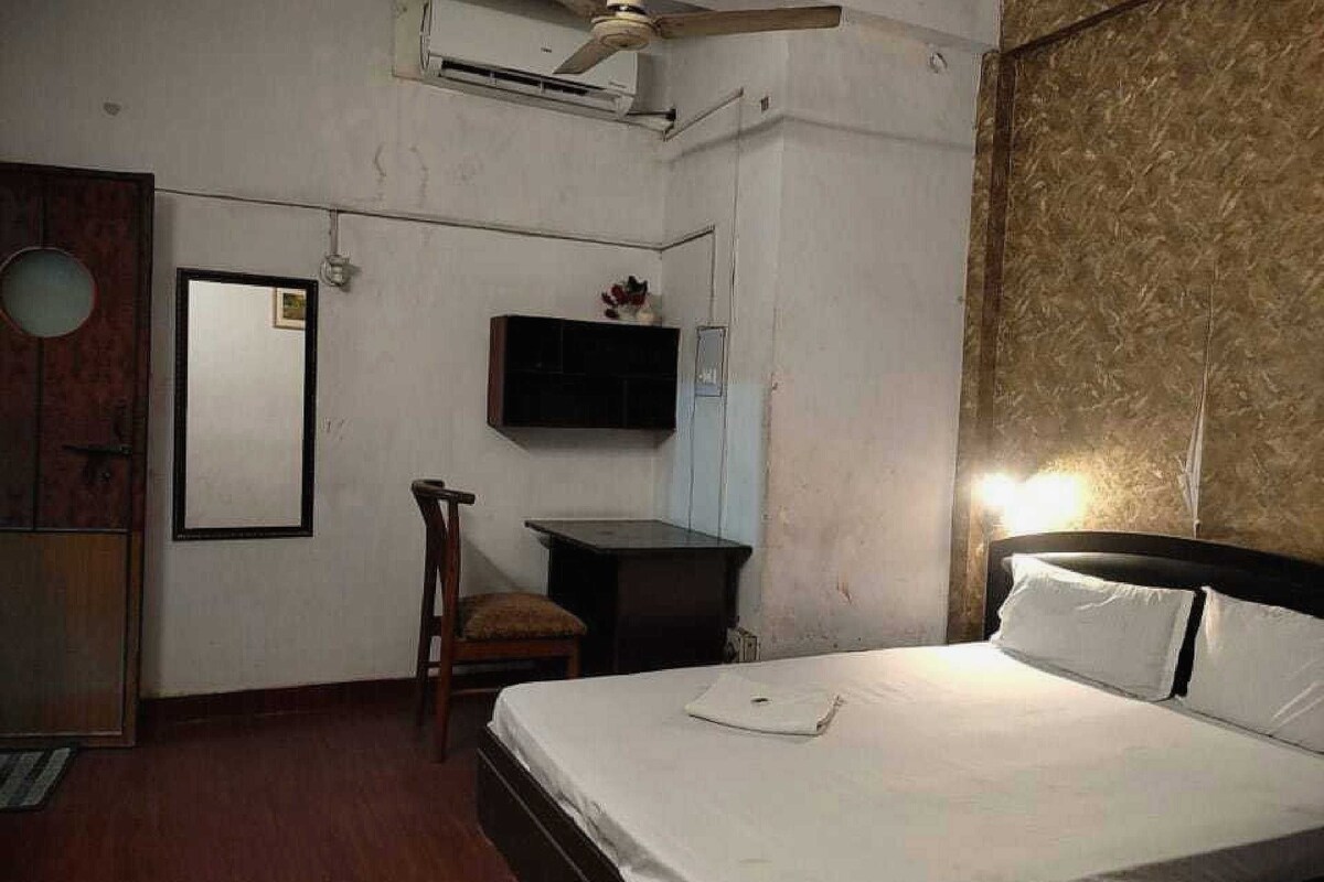 Een slaapkamer met een bed, een bureau, een stoel, een airconditioning en een televisie aan de muur.