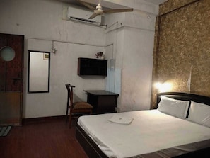 Een slaapkamer met een bed, een bureau, een stoel, een airconditioning en een televisie aan de muur.
