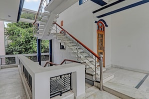 A staircase with a metal handrail and a wooden handrail, leading to a door with a geometric pattern. - Hotel O Shiva Grand (Lucknow)