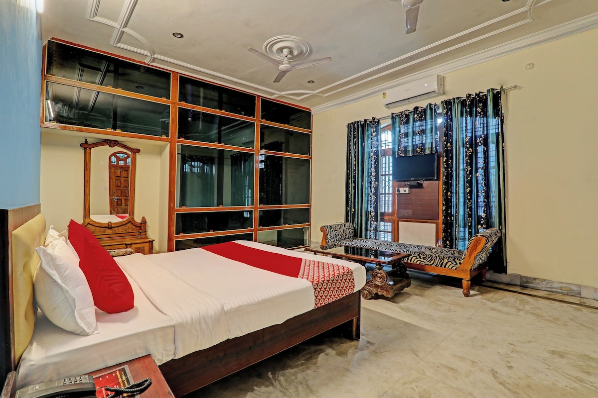 A bedroom with a large bed, a wooden dresser, a mirror, a television, and a window with curtains.