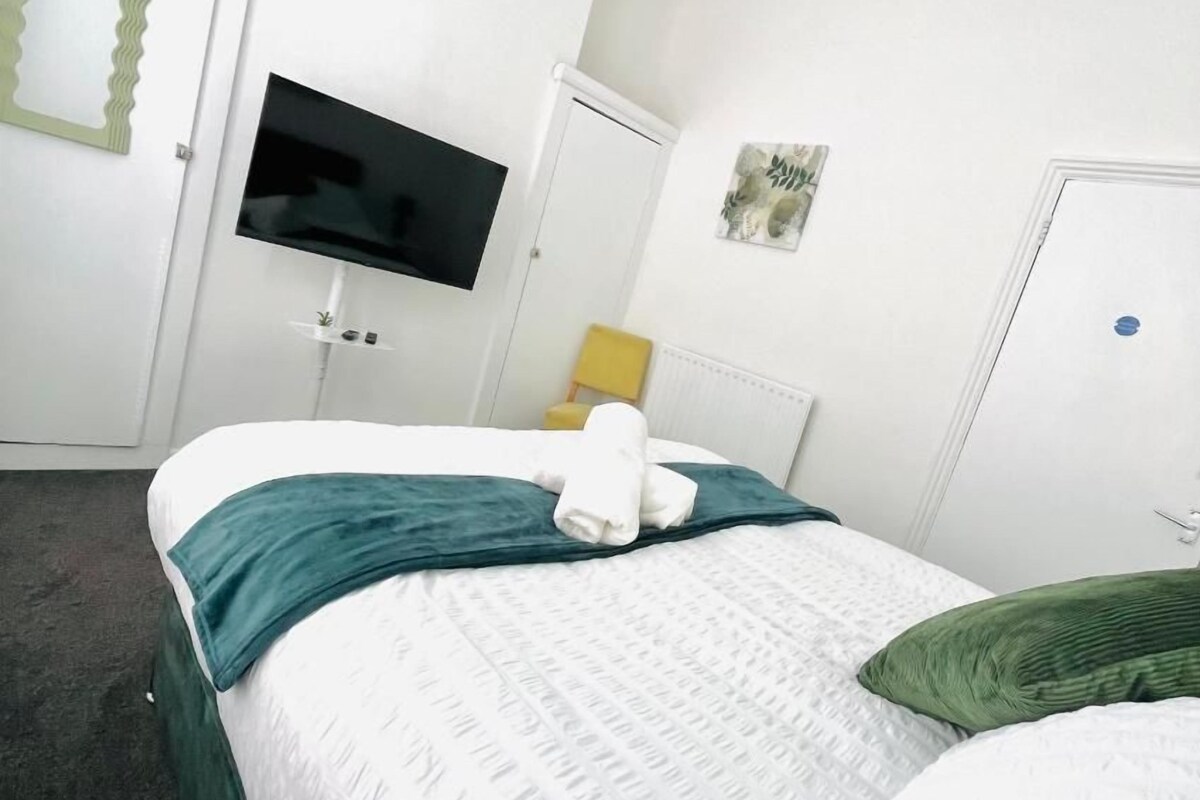 Een hotelkamer met een bed, een aan de muur bevestigde televisie, een deur en een kleine tafel met een plant.