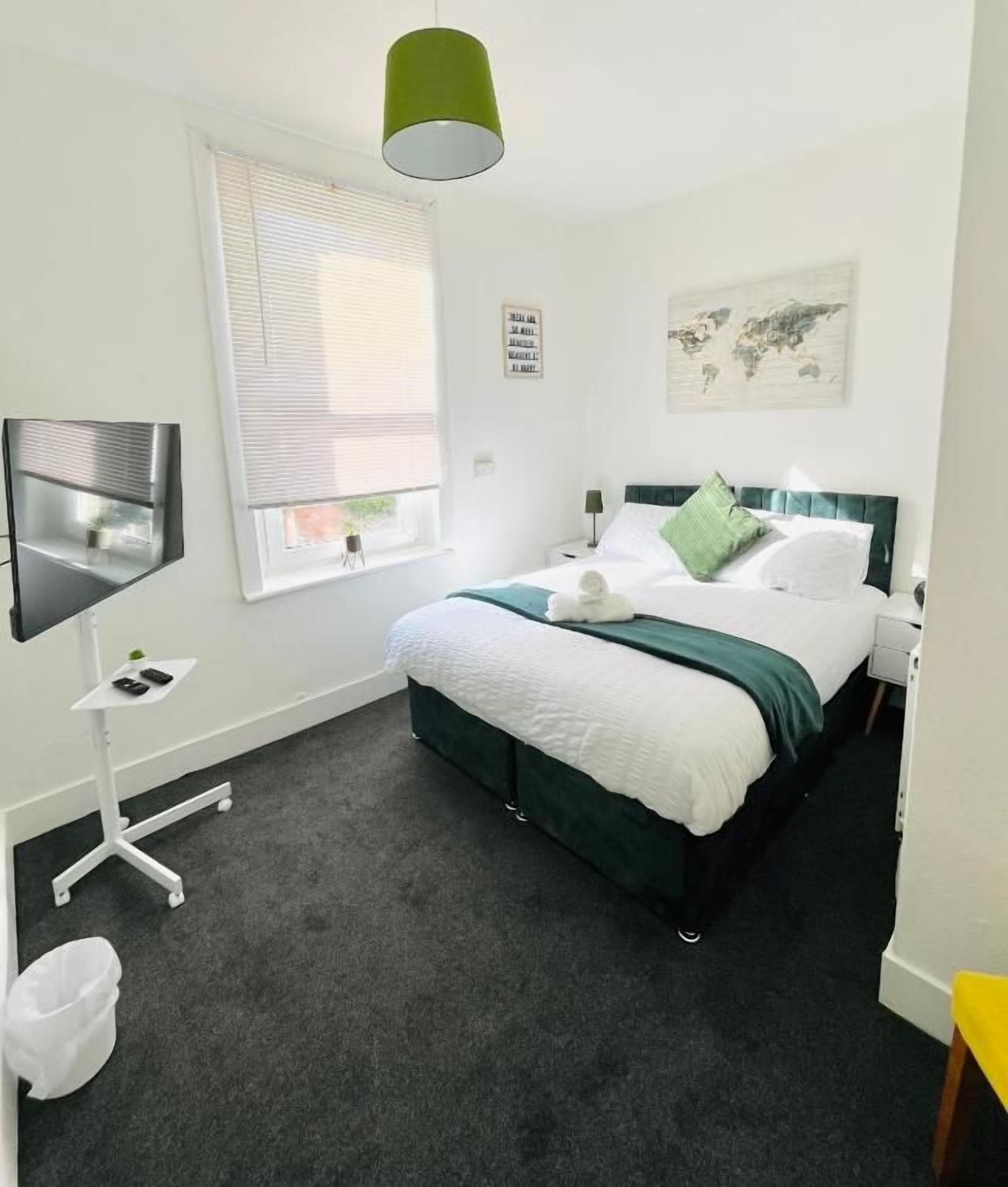 Habitación de hotel con cama, escritorio, silla, televisor y ventana con persianas.