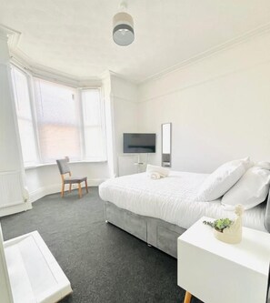 Een slaapkamer met een bed, een stoel, een televisie en een raam.