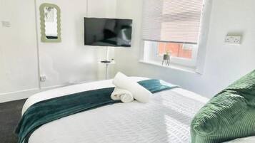 Una habitación de hotel con cama, televisión, ventana con persianas y una lámpara colgante verde.