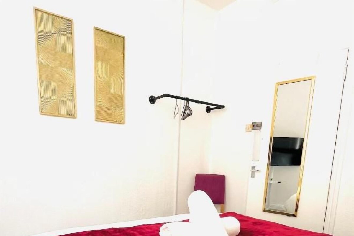 Een hotelkamer met een bed, een rode deken, een witte handdoek, een spiegel en twee kunstwerken aan de muur.