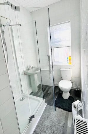 Een badkamer met een douchecabine van glas, een wit wastafelmeubel en een toilet.