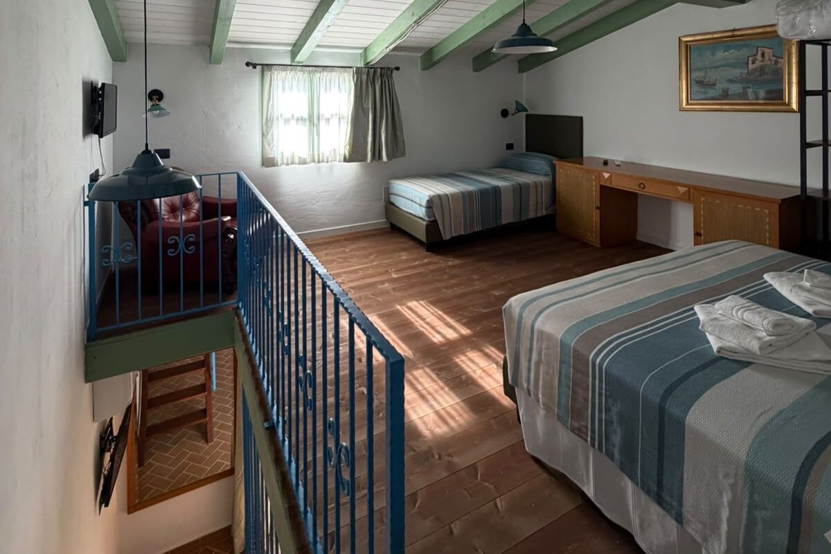 A bedroom with a loft area, a bed, a desk, and a window with curtains.