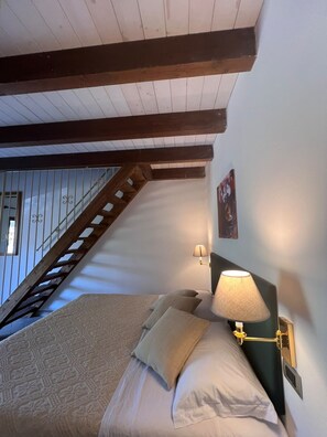A bedroom with a bed, a nightstand, a lamp, a wall-mounted picture, and a wooden staircase. - Agriturismo Bed Breakfast Tanca Taroni (Sardegna)