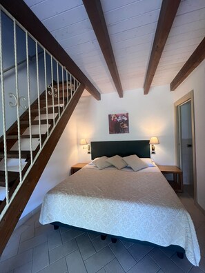 A bedroom with a bed, a headboard, a painting, a staircase, and a nightstand with a lamp. - Agriturismo Bed Breakfast Tanca Taroni (Sardegna)