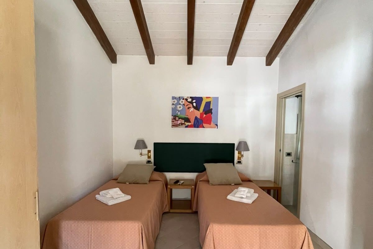 A hotel room with two beds, a painting on the wall, and a wooden ceiling.