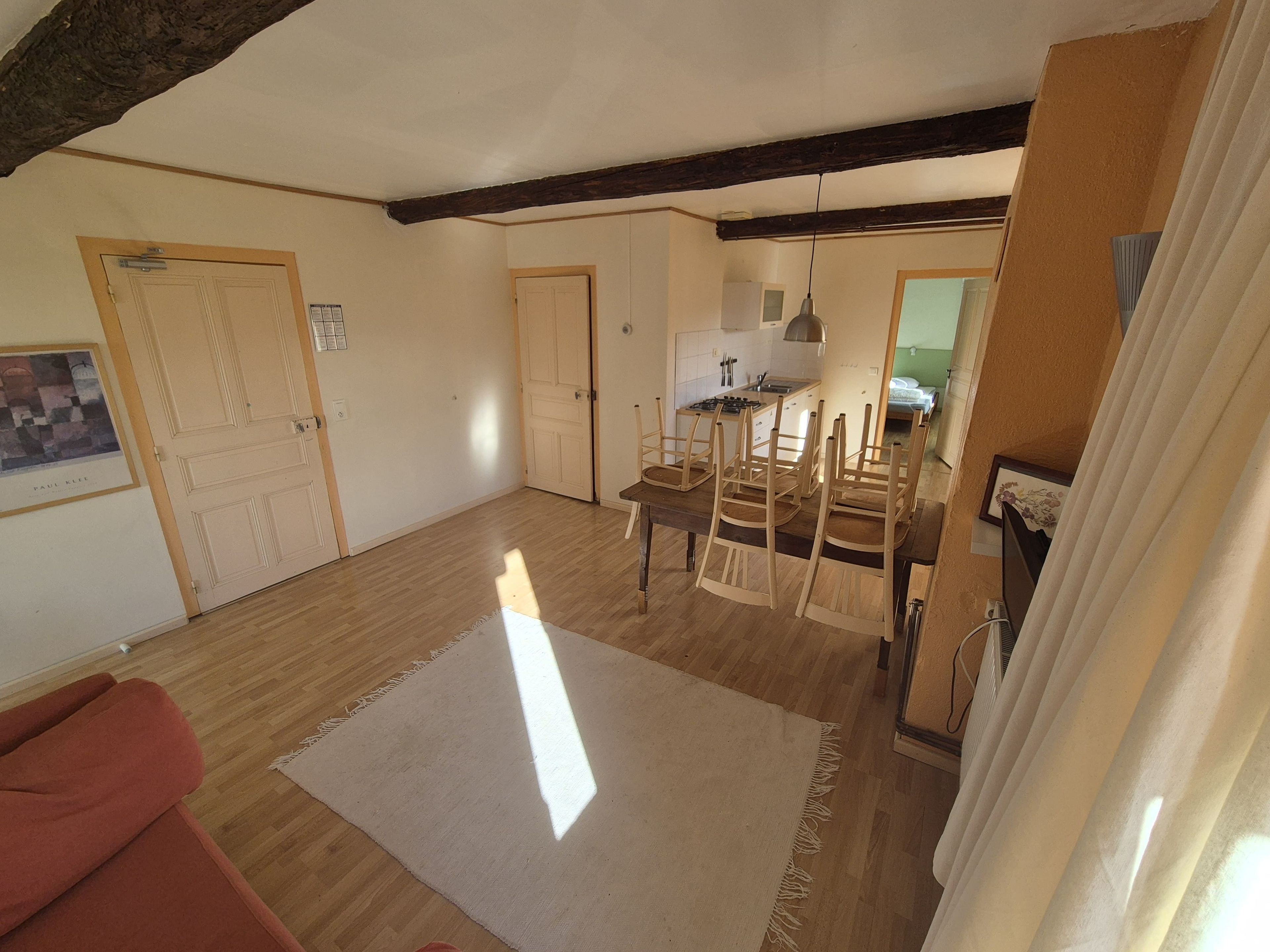 Amplia sala de estar con piso de madera, una mesa de comedor con sillas, una zona de cocina y un ventanal que deja entrar luz natural.