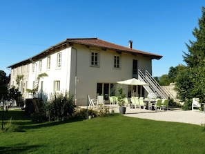 A two-story building with a tiled roof, a staircase leading to the upper floor, and outdoor seating with umbrellas.