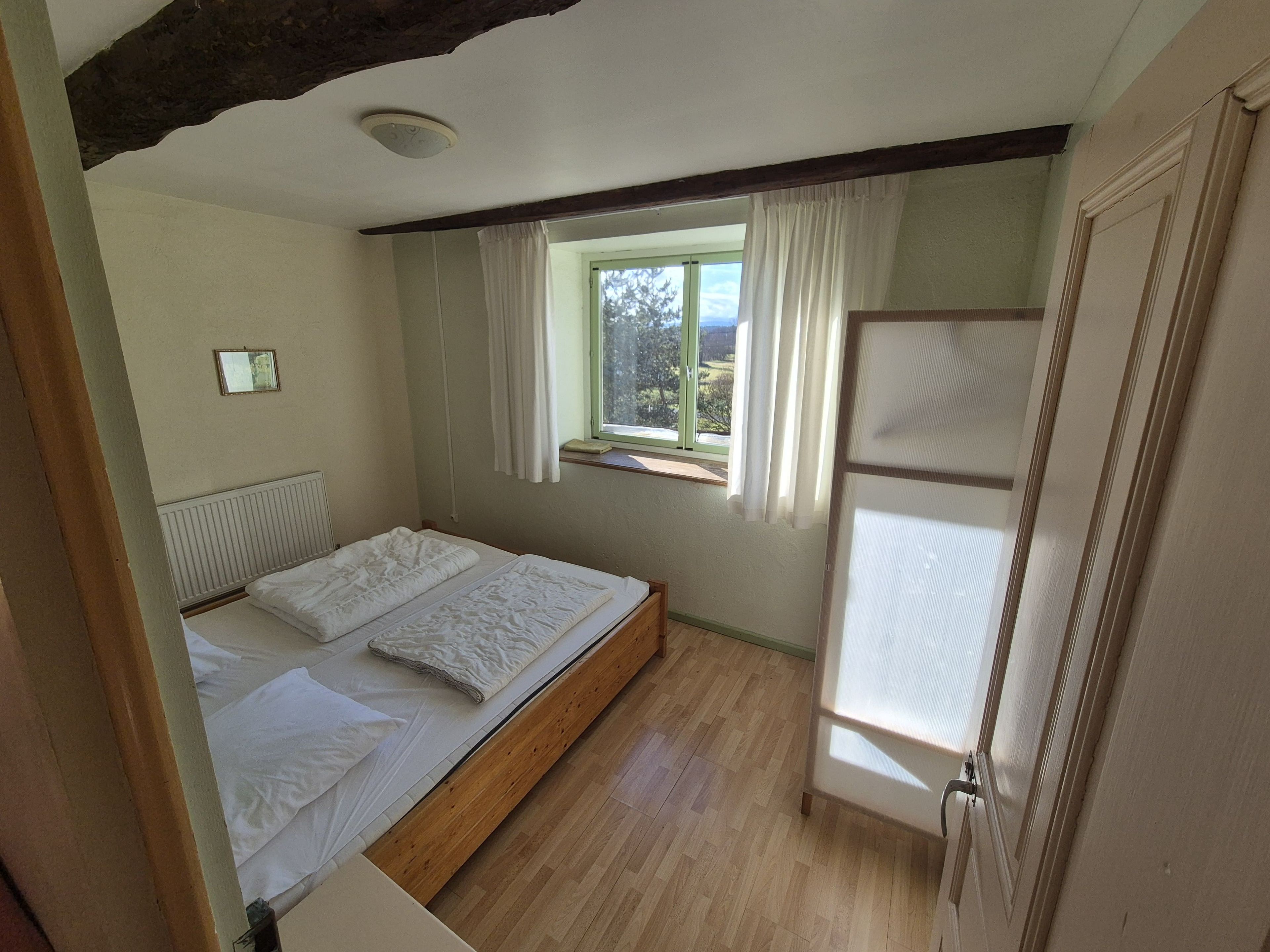 Een slaapkamer met een houten bed, een raam met gordijnen en uitzicht op de omgeving.