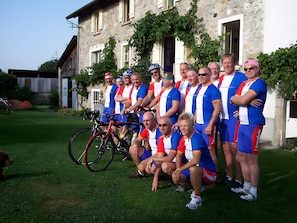 Eine Radsportgruppe in Uniform posiert vor einem Steinhaus mit einem grünen Rasen.