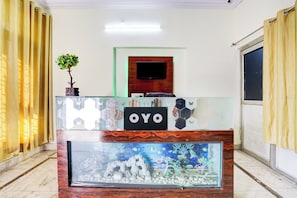 A reception area with a glass desk, a potted plant, a sign with 'OYO', a flat-screen TV, and an aquarium. - Hotel O Gharaunda (Lucknow)