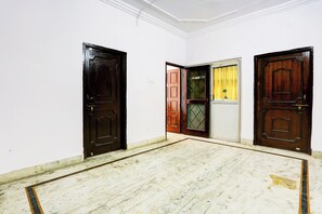 A room with three wooden doors, one of which is open revealing a yellow curtain. - Hotel O Gharaunda (Lucknow)