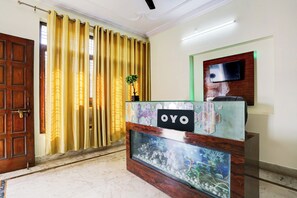 A reception desk with a nameplate, a television mounted on the wall, and a door with a curtain. - Hotel O Gharaunda (Lucknow)