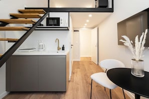 A modern kitchen with a built-in microwave, a coffee maker, and a sink. There is a staircase with wooden steps leading to a landing. A black table with a vase of white flowers is visible. - K20 - Boutique Apartments by BQA (Budapest)