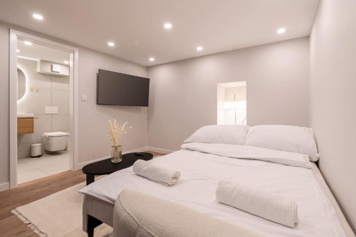 A modern bedroom with a bed, bedside table, and a TV mounted on the wall.