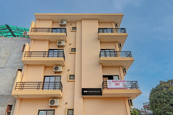 Un edificio de varios pisos con balcones, unidades de aire acondicionado y un letrero que indica una propiedad llamada 'Madhurima Inn'.