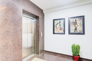 Un ascensor con pared de granito, dos cuadros enmarcados y una planta en maceta.