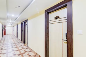 Un pasillo de hotel con varias puertas, piso estampado e iluminación empotrada en el techo.