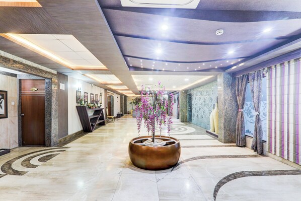 Un vestíbulo de hotel con una recepción, una gran maceta decorativa con flores y un suelo estampado.