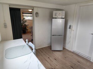Habitación compacta con cama, refrigerador y puerta que da a otra zona.