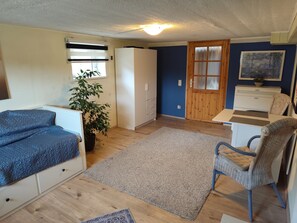 Quarto pequeno com cama, escrivaninha, cadeira, guarda-roupa, planta e porta com janela.