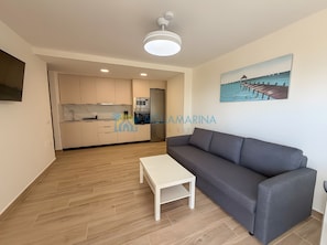 A modern living room with a grey sofa, a white coffee table, and a kitchen in the background.