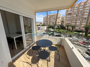 A balcony with a table and chairs, a sliding glass door, and a view of a residential area with buildings and palm trees.
