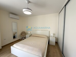 A bedroom with a bed, bedside tables, a mirror, an air conditioning unit, and a wall-mounted ceiling light.