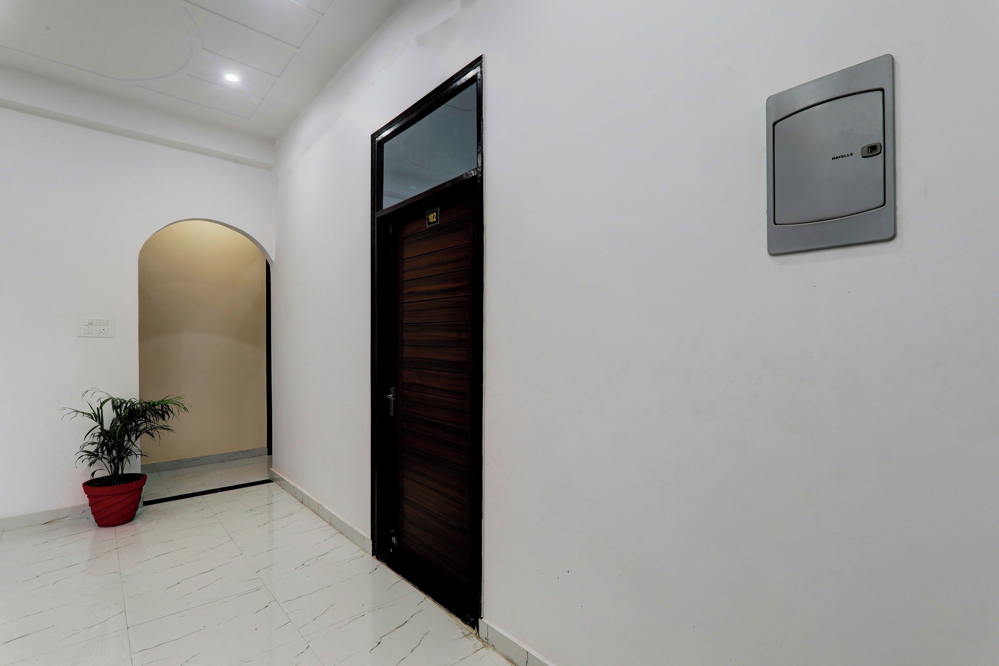 Un pasillo con una puerta cerrada, una planta en maceta y un interfono en la pared.