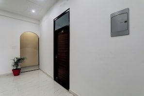 A hallway with a closed door, a potted plant, and a wall-mounted intercom. - Hotel O A B Hotels (Lucknow)
