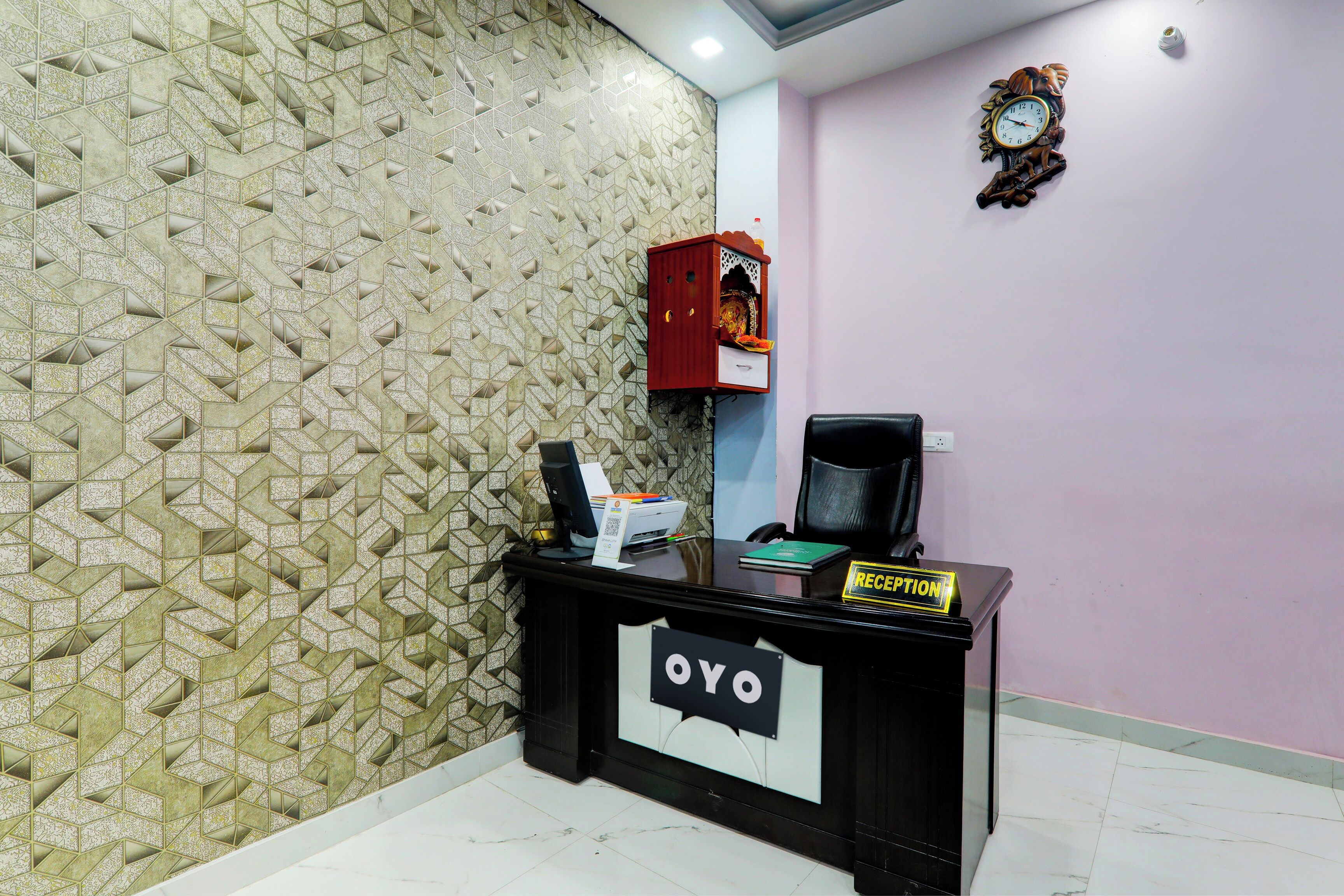 Una mesa de recepción con un cartel que dice 'Reception', una computadora, una impresora y un reloj decorativo en la pared.