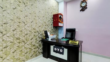 Una mesa de recepción con un cartel que dice 'Reception', una computadora, una impresora y un reloj decorativo en la pared.