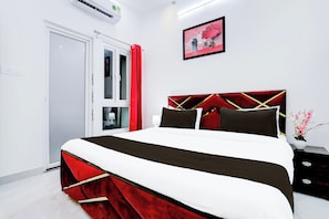 A hotel room with a bed, a bedside table, a nightstand, a wall-mounted picture, and a door. - Hotel O Virat Inn (Lucknow)