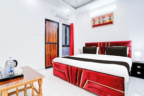A hotel room with a bed, a table with a kettle and cups, a red and white bedspread, a red headboard, a painting on the wall, and a window with a view. - Hotel O Virat Inn (Lucknow)