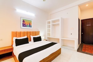 Habitación de hotel con una cama, pared blanca, un cuadro, cabecera de madera y una puerta.