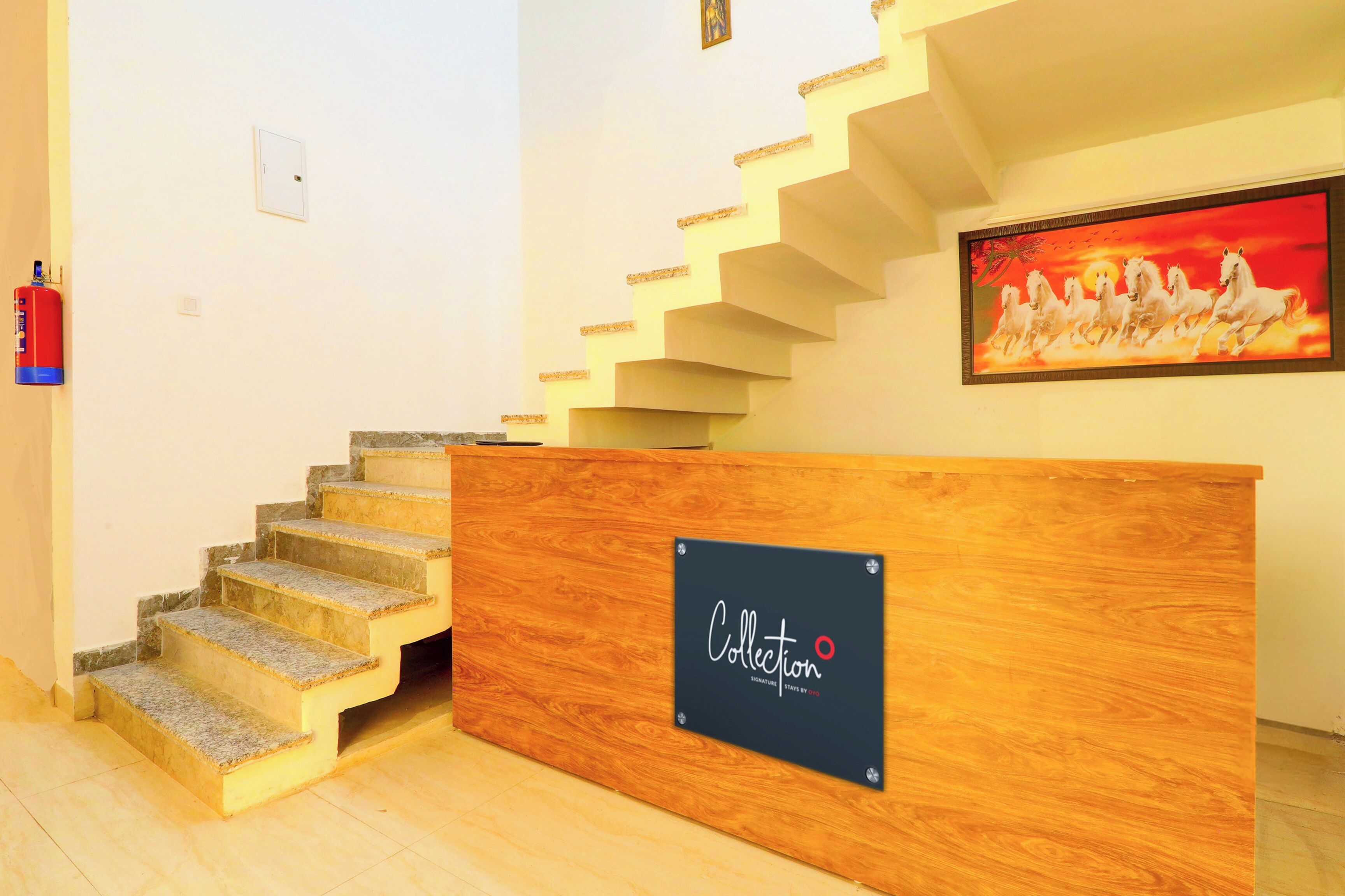 Una escalera con un mostrador de recepción de madera en el centro, un extintor en la pared y un cuadro de caballos en la pared.