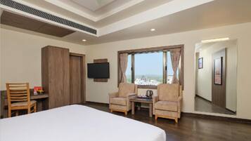 A hotel room with a large bed, two armchairs, a small table, a TV, and a window with a view.